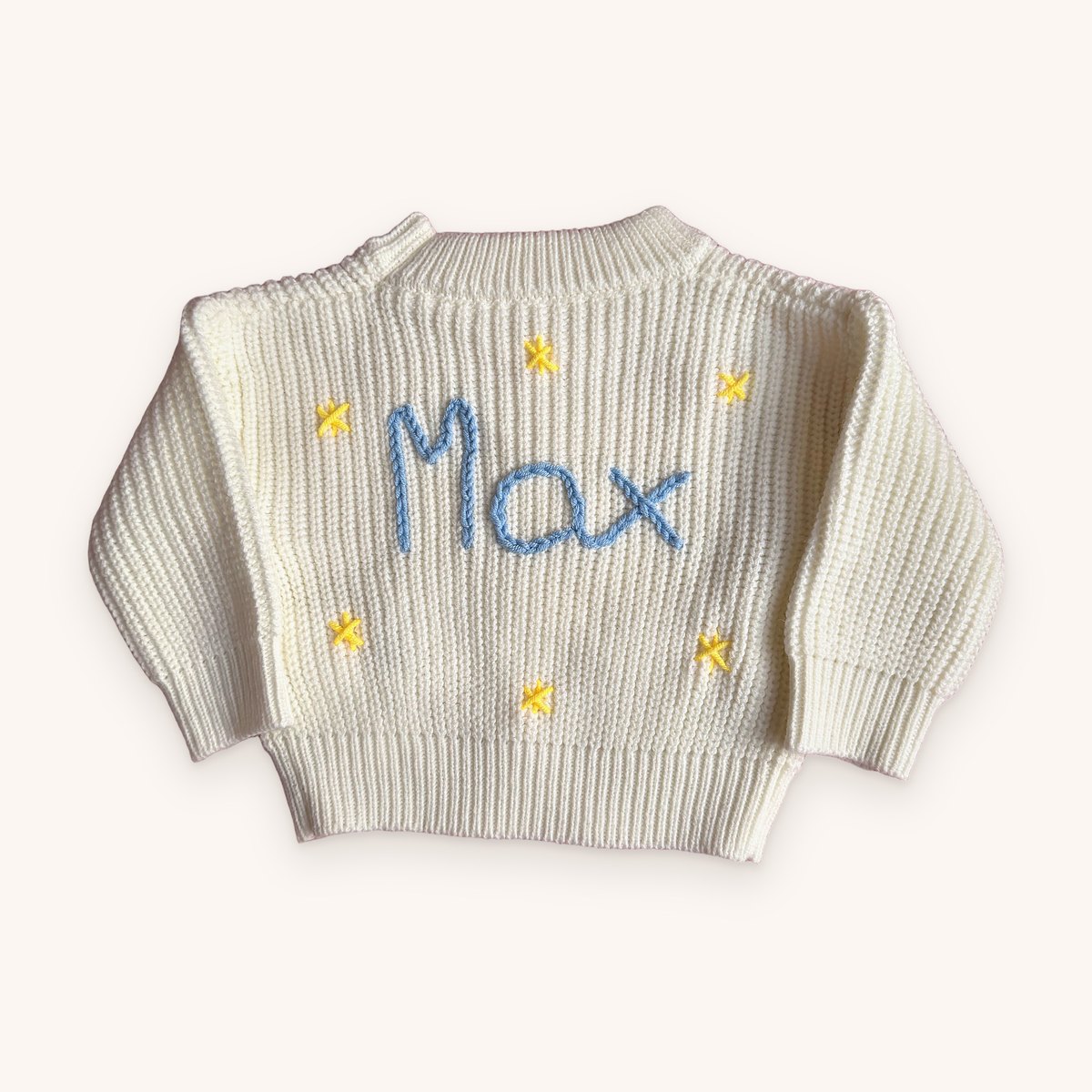 Cream chunky knit baby jumper with the name Max hand-embroidered in blue chain stitch, surrounded by little yellow cross-stitch stars